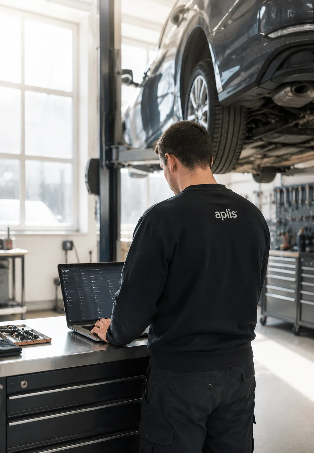 Person in dunkelgrüner Arbeitskleidung arbeitet am Laptop auf der Werkstatttheke